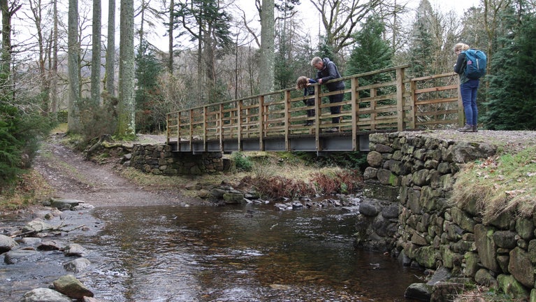 A family play pooh sticks on a bridge while walking the River Esk trail on a cloudy winter's day